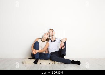 Ein Paar sitzt auf einem weichen Teppich vor einer weißen Wand in einer entspannten Umgebung Stockfoto