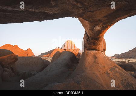 Blick auf warmes Licht, das die zerklüfteten, sonnenverwöhnten Felsformationen in einer weiten, trockenen Landschaft unter klarem Himmel küsst und einen starken Kontrast von Schatten und erzeugt Stockfoto
