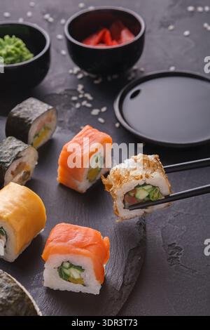 Sushi-Collage mit verschiedenen Rolls und Dip-Saucen auf dunkler Oberfläche Stockfoto