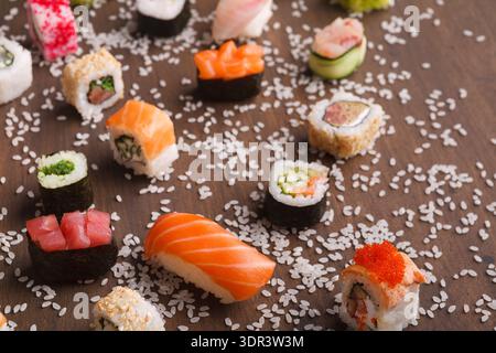 Sammlung von Sushi-Stücken, die auf einer Holzfläche angeordnet sind, mit verstreutem Reis Stockfoto