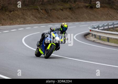 Dreiviertelansicht eines blau-neongelben Sportmotorrads in einer scharfen Kurve auf einer Bergstraße. Stockfoto