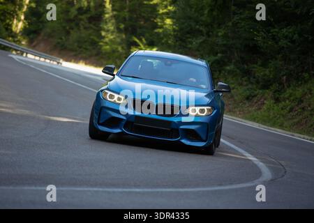 Dreiviertelansicht eines blauen Performance-Sportwagens, der schnell durch eine scharfe Kurve auf einer asphaltierten Bergstraße fährt. Stockfoto