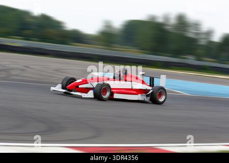 Schneller roter und weißer Rennwagen mit offenem Rad, der während eines Renntages auf einer professionellen Strecke mit Bewegungsunschärfe beschleunigt. Stockfoto