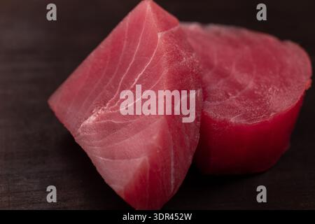 Zwei rohe Thunfischsteaks zeigen eine leuchtende rote Farbe und eine zarte Textur vor dunklem Hintergrund, die frische Meeresfrüchtezutaten für ein gesundes Kochen repräsentieren. Stockfoto