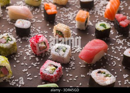 Sammlung von Sushi-Stücken auf einem Holzbrett mit verstreuten Reiskörnern Stockfoto