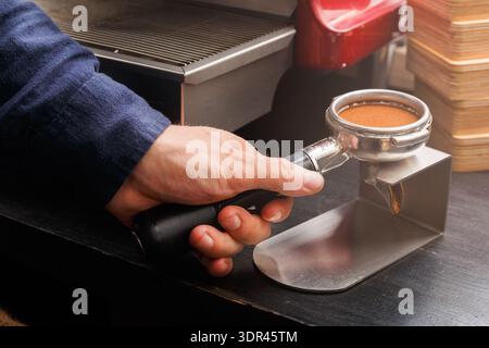 Hand hält Kaffeeportafilter in der Nähe der Espresso-Maschine im lebhaften Café während der morgendlichen Rush Hour Stockfoto