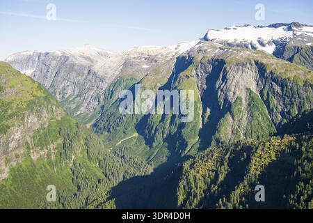 Aus der Vogelperspektive auf die zerklüfteten, grünen Berge treffen auf den klaren blauen Himmel, mit schneebedeckten Gipfeln im Kontrast zu den tiefgrünen Tälern in Sitka, Alaska Stockfoto