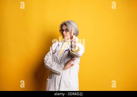 Leitende Ärztin mit Stethoskop, die mit ihrem angehobenen Finger eine Stoppgeste macht Stockfoto