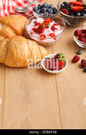Bäckereikollektion mit Croissants, Joghurt und frischen Beeren auf Holztisch Stockfoto
