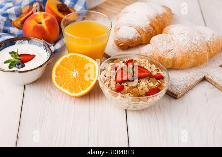 Frühstück mit Obst, Joghurt, Müsli und Croissants auf einem Holztisch Stockfoto