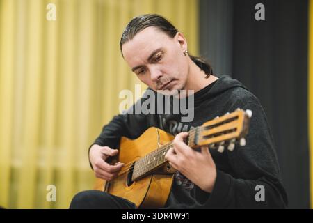 Ein Mann spielt eine akustische klassische Gitarre auf gelbem Bühnengrund. Stockfoto
