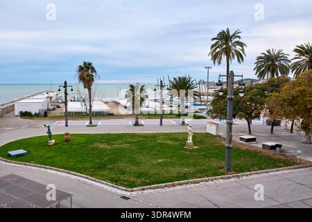 Sitges. Spanien - 17. Februar 2026: Palmengesäumte Promenade und Yachthafen mit verankerten Segelbooten entlang der Mittelmeerküste in Katalonien unter ruhiger Lage Stockfoto