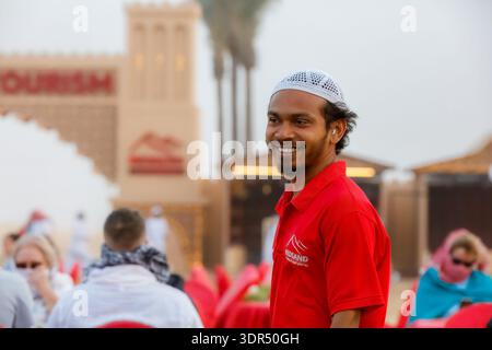 Dubai, Vereinigte Arabische Emirate, 9. März 2025: Mitarbeiter in rotem Hemd und weißer Mütze interagieren mit Gästen in einem Außenbereich in einem Wüstentourismus Stockfoto
