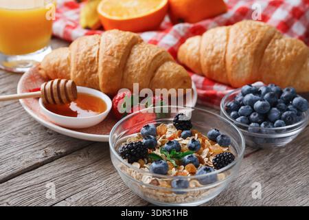 Frühstück mit Croissants, Joghurt, Obst und Honig auf einem Holztisch Stockfoto