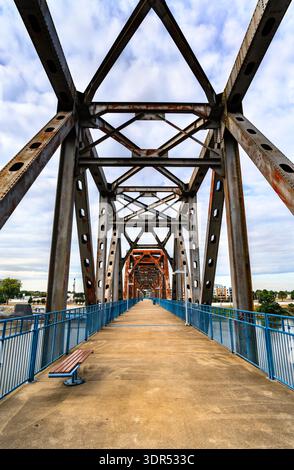 Clinton Presidential Park Bridge in Little Rock, Arkansas. Die historische, umfunktionierte Eisenbahnbrücke verfügt über ein rostiges Stahlfachwerk und blaue Geländer über den Arkansas River Stockfoto