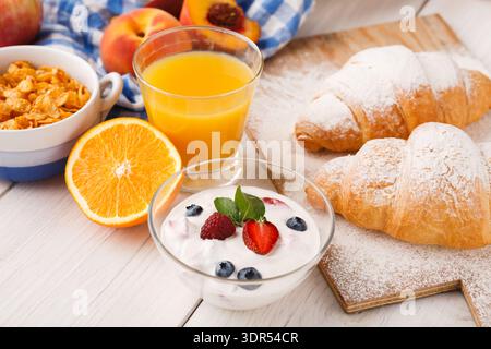Frühstück mit Croissants, Joghurt, Orangensaft und Obst auf einem Holztisch Stockfoto
