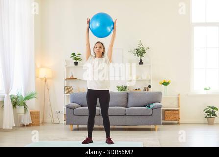 Aktive Passform alte sportliche Seniorin, die zu Hause mit Fitnessball trainiert, Dehnungsübungen macht Stockfoto