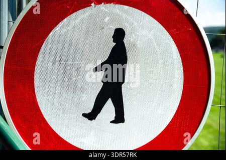 Eine Nahaufnahme eines runden rot-weißen Verbotsschildes mit einer schwarzen Silhouette eines Wandermannes, montiert auf einem Metallzaun im Freien. Stockfoto