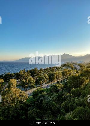Küstenblick von Antalya mit Mittelmeer, grünem Park und Taurusgebirge zur goldenen Stunde, Türkei. Stockfoto