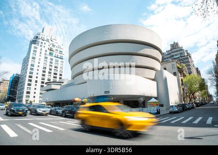 New York City, 15. Mai 2023: Berühmtes Guggenheim Museum, mit einem gelben Taxi, das auf einer belebten Straße vorbeizieht Stockfoto