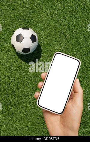 Hand hält das Smartphone unter dem Fußballfeld mit Ball. Stockfoto