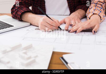 Zwei Personen arbeiten zusammen an Architekturplänen in einem Büro während der Tageslichtstunden Stockfoto