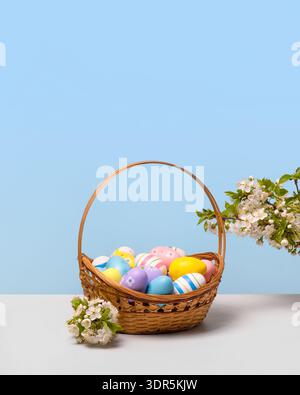 Bunte Ostereier in einem Korb mit Frühlingsblumen: Blühende Frühlingskirschzweige auf grauem Tisch. Osterkonzept Stockfoto