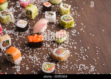 Sammlung von Sushi-Stücken, die auf einer Holzfläche angeordnet sind, mit verstreutem Reis um sie herum Stockfoto