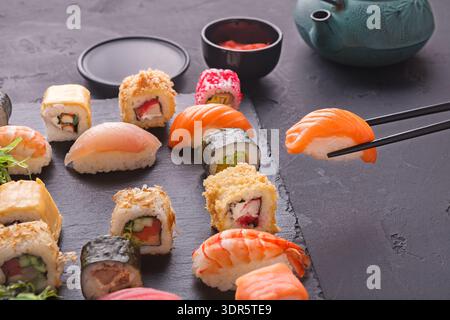 Sammlung von Sushi-Stücken auf einer schwarzen Schieferplatte mit Utensilien und Sauce Stockfoto