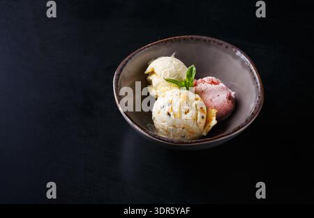 Drei Schaufeln Eiscreme in einer Schüssel mit einem Minzzweig auf dunklem Hintergrund Stockfoto
