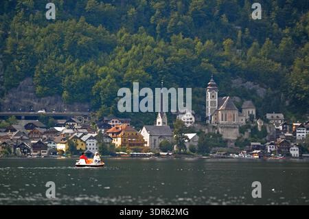 Hallstätter Dorf am Hallstätter See, Oberösterreich, mit Touristen auf Tretbooten und Kirchtürmen vor alpiner Waldkulisse. Stockfoto