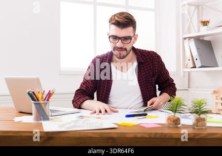 Mann, der tagsüber am Schreibtisch mit Papieren und Laptop arbeitet, im Home Office Workspace Stockfoto