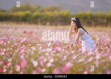 Seitenansicht einer jungen Frau in Sommerkleid und Sonnenbrille auf dem Kopf, die bei Sonnenuntergang in einem Blumenfeld steht Stockfoto