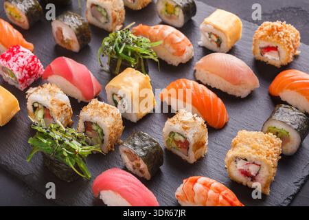 Sushi-Kollektion auf einer schwarzen Platte, die verschiedene Arten und Farben von Sushi-Rollen zeigt Stockfoto
