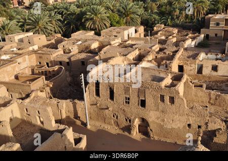Blick aus einem hohen Winkel über die alten Schlammsteinruinen des Dorfes Al Qasr vor dem Hintergrund von Dattelpalmenhainen, Dakhla Oase, Ägypten. Stockfoto
