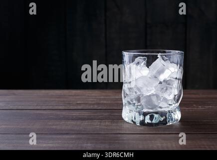 Glas gefüllt mit Eiswürfeln auf einem Holztisch vor dunklem Hintergrund Stockfoto