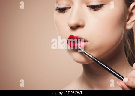 Tragen Sie den roten Lippenstift mit einem Pinsel auf, um einen Make-up-Look in einer Beauty-Umgebung zu erhalten Stockfoto