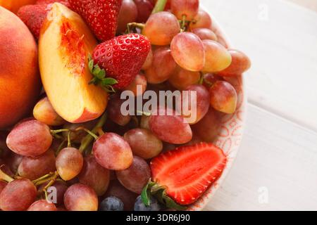 Frisches Obst auf einem Teller mit Erdbeeren, Trauben und Pfirsichen im Sonnenlicht Stockfoto