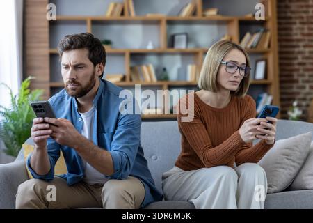 Ein Paar, das zu Hause auf einer Couch sitzt und sich ignoriert, während es in ihr Smartphone vertieft ist, zeigt Kommunikationsstörungen und Technologiesuchtige Stockfoto