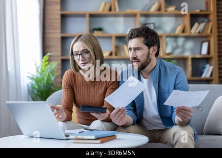 Stressiges Paar, das Rechnungen und Finanzdokumente zu Hause überprüft, Ausgaben auf einem Laptop und Rechner berechnet, mit Kreditkartenschulden zu kämpfen hat und Stockfoto
