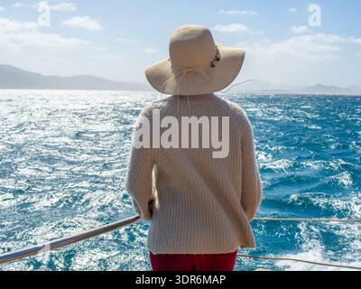 Rückansicht einer Frau, die einen Hut trägt und auf dem Meer segelt Stockfoto