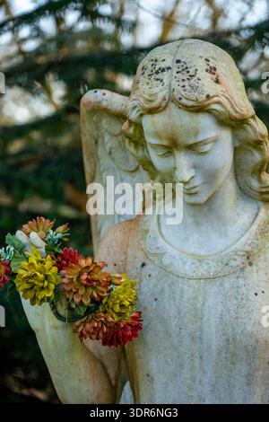 stone statue of an angel holding a bunch of fresh colourful flowers in a cemetery on the isle of wight, UK Stockfoto