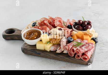 Nahaufnahme einer Wurstplatte mit Salami, Käse, Oliven, Marmelade, Nüssen und Heidelbeeren auf rustikalem Holzbrett. Stockfoto