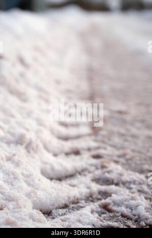 Vertikale Nahaufnahme von überfülltem, hellem Schnee und schlammigem Eis an einer Straße oder Einfahrt, die sich wiederholende Reifenspurkämme und granulares kristallines Textu freigibt Stockfoto