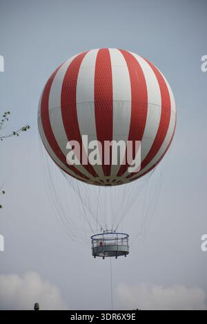 Rot-weiß gestreifter Heißluftballon mit Passagierkorb im klaren Himmel. Luftfahrt und Tourismus im Freien. Stockfoto