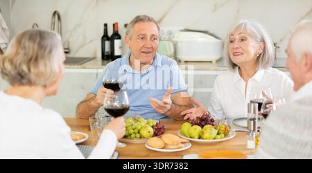 Zwei ältere Ehepaare sitzen am Tisch, genießen Essen und Wein, plaudern. Stockfoto
