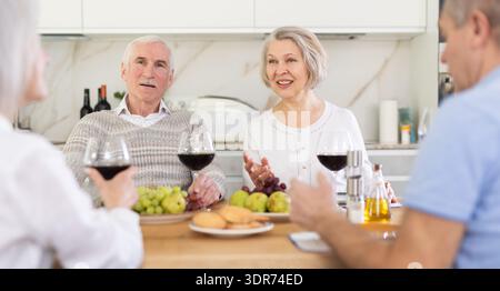 Eine Gruppe glücklicher älterer Menschen trinkt Rotwein und plaudert am festlichen Tisch Stockfoto