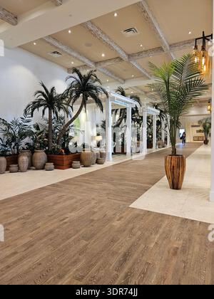 NUR REDAKTIONELLE VERWENDUNG - MARGARITAVILLE RESORT HOLLYWOOD BEACH FLORIDA: Der Innenkorridor und der Loungebereich des Margaritaville Hollywood Beach Resort in Florida. Der Raum verfügt über weiß getünchte Holzbalken, Bodenbeläge in Naturholzoptik und eine Reihe von „Cabanas“ im Innenbereich mit weißen Pergolen und Vorhängen. Große tropische Palmen in übergroßen Steinpflanzen säumen den Flur und schaffen eine tropische Atmosphäre im Innen- und Außenbereich. Warme, bernsteinfarbene Pendelleuchten und klare weiße architektonische Linien prägen diesen luxuriösen Gastfreundschaftsbereich an der Küste. Stockfoto