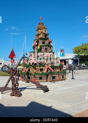 NUR FÜR REDAKTIONELLE ZWECKE: KEY WEST FLORIDA: Nautischer Weihnachtsbaum aus Hummerfallen, Key West Historic Seaport. Ein großer Weihnachtsbaum aus gestapelten Holzfallen, dekoriert mit Grün, roten Bögen und Bojen. Ein großer rostiger Anker sitzt im Vordergrund an der Uferpromenade. Stockfoto