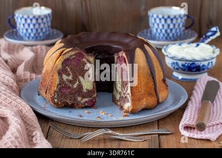 Tisch mit Marmorkuchen mit Kirschen, Schokoladenglasur und Porzellan Stockfoto